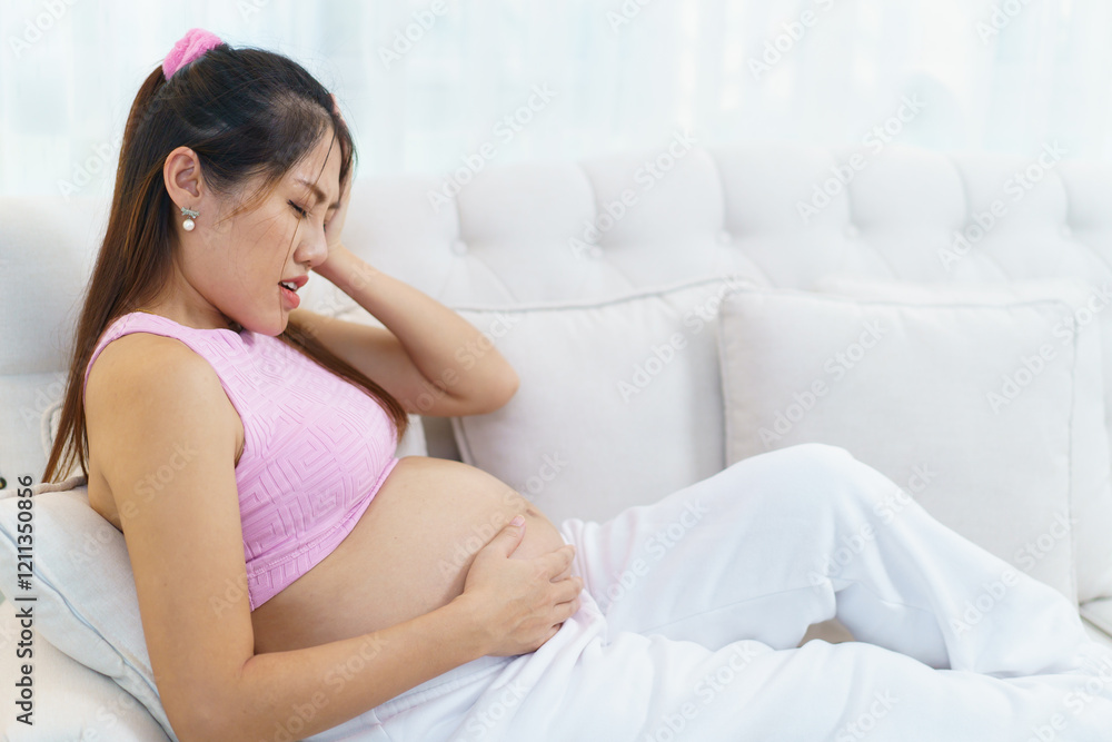 Concerned Asian heavily pregnant woman sitting on sofa in living room. Concerned Asian heavily pregnant woman sitting on sofa in living room.