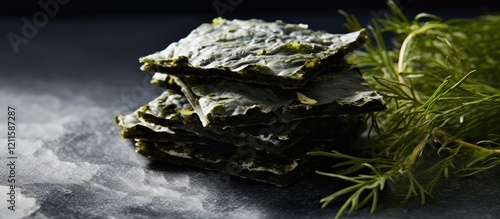 Crispy nori seaweed sheets stacked on a dark grey surface with fresh herbs in the background showcasing a healthy Japanese snack option