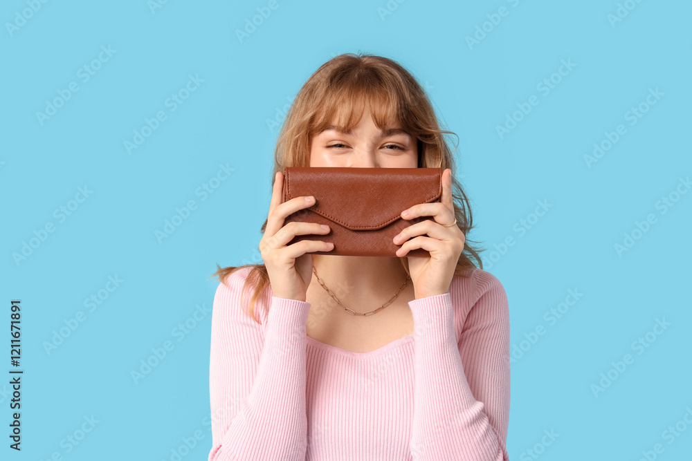 Young woman covering mouth with wallet on blue background Young woman covering mouth with wallet on blue background