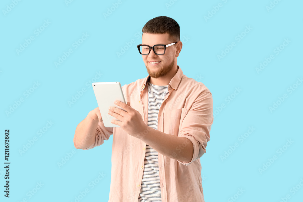 Young man in eyeglasses using tablet computer on blue background Young man in eyeglasses using tablet computer on blue background