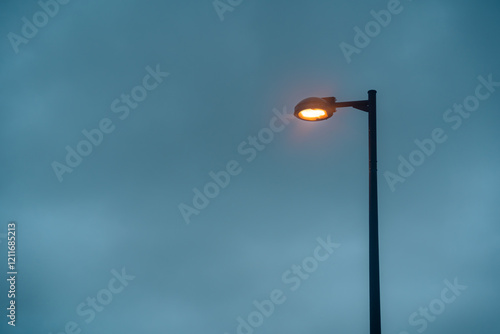 Modern street lamp is turning on with orange light, isolated by dark cloudy sky. Took during summer season in Naha, Okinawa, Japan. Perfect for graphic resource, background or wallpaper