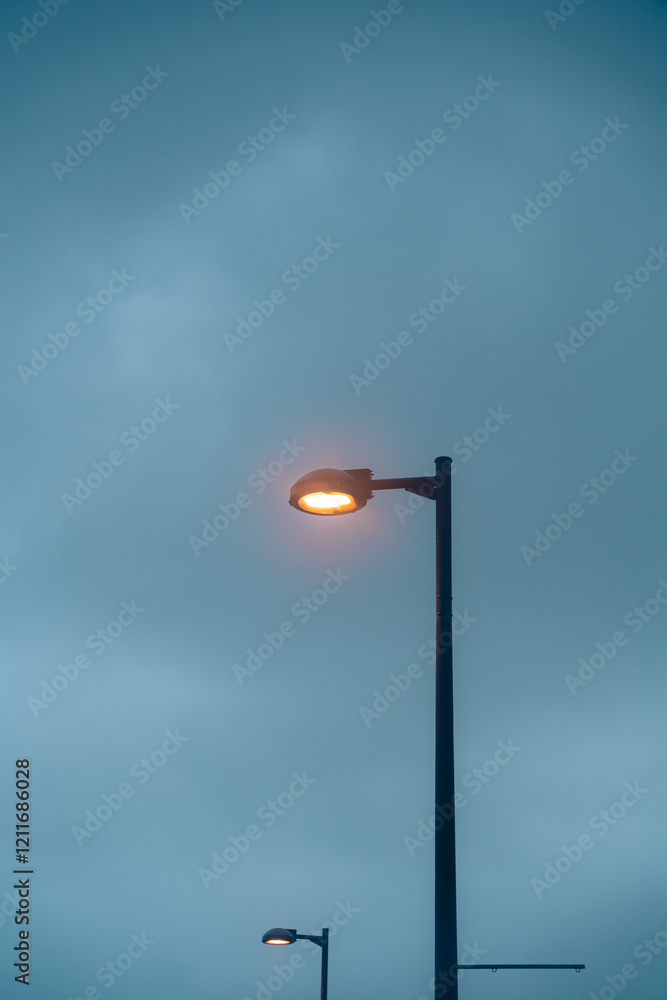 Modern street lamp is turning on with orange light, isolated by dark cloudy sky. Took during summer season in Naha, Okinawa, Japan. Perfect for graphic resource, background or wallpaper Modern street lamp is turning on with orange light, isolated by dark cloudy sky. Took during summer season in Naha, Okinawa, Japan. Perfect for graphic resource, background or wallpaper