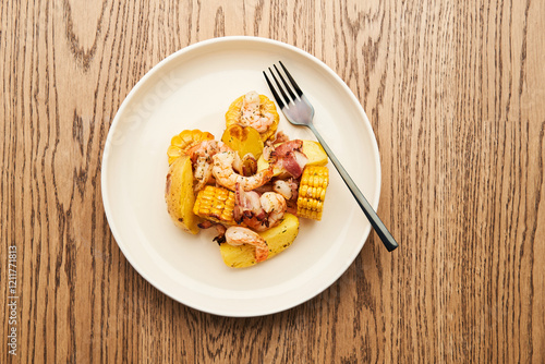 A plate holds a savory blend of shrimp, corn, and potatoes, seasoned perfectly. The meal is set on a wooden table, inviting and ready to enjoy photo