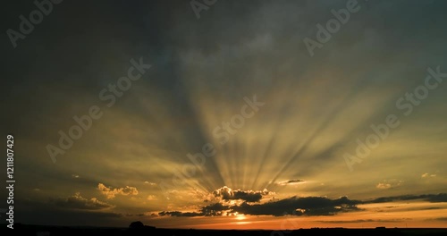Timelapse of the wide angle dark and orange sunset sky with sun shining through the clouds on the horizon and distinctive rays of light extending toward the camera