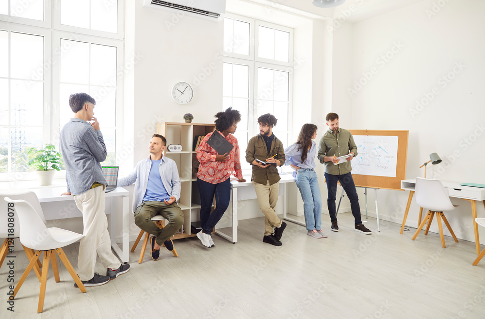 Fototapeta premium Diverse team of business people engages in a conversation during a meeting or training session in the office. Group focuses on teamwork, collaboration, and professional development in the workplace.