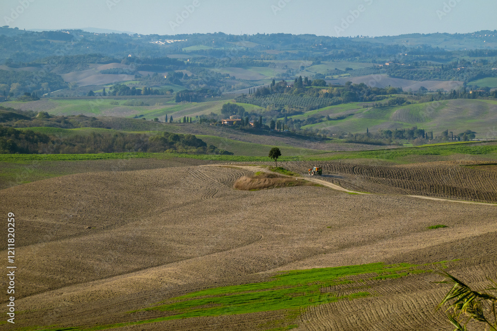 Sprawling rural scenery featuring open fields, a lone tree, distant farm buildings, and a vehicle. Sprawling rural scenery featuring open fields, a lone tree, distant farm buildings, and a vehicle.