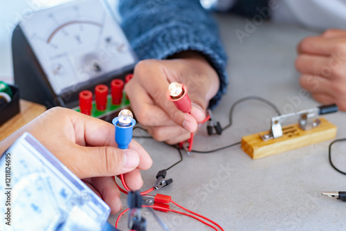 Children are studying electrical circuit systems by experimenting with electrical connections using a small electric meter and a small flashlight bulb in physics science class, soft focus. photo