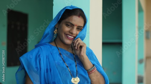 A pretty married woman in traditional wear smiling and looking at the camera - village lady  rural concept  desi lifestyle  ethnic style. The shot of the village lady standing near the wall and pos... photo