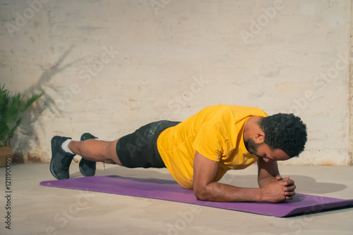 A dedicated man consistently performs a challenging plank exercise on a bright purple yoga mat in an indoor setting