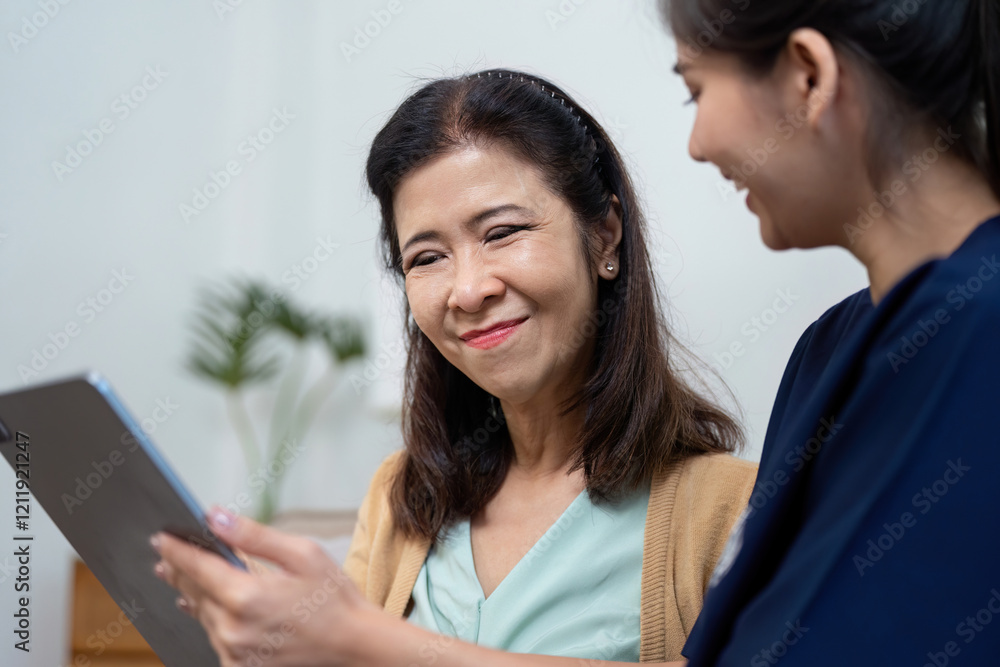 Elderly patient smiling while reviewing health information with caregiver on tablet Elderly patient smiling while reviewing health information with caregiver on tablet