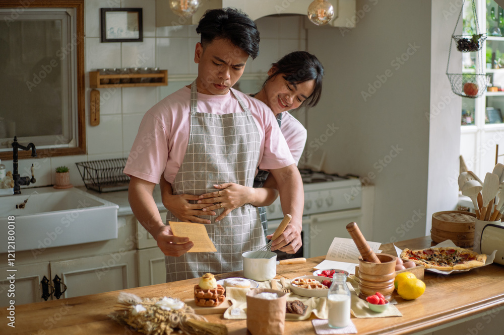 A cheerful Asian couple in matching checkered aprons enjoying a playful cooking moment in a cozy kitchen. They prepare food together, surrounded by waffles, strawberries, milk, and pizza