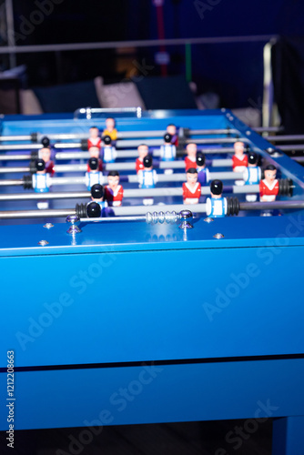 blue foosball table in focus, showcasing detailed player figurines arranged in red and blue teams. The scene captures the lively essence of recreational and social gaming, set in an inviting indoor photo