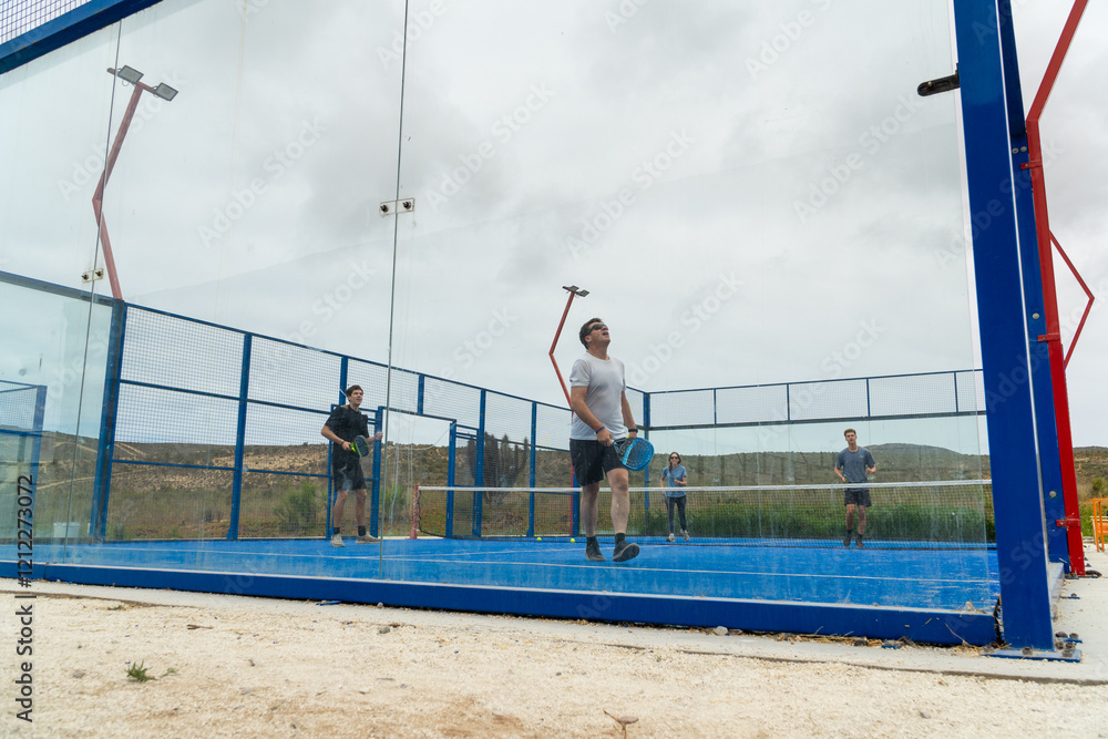 A joyful family playing padel on an outdoor court, capturing their moments of fun and togetherness under the cloudy sky.