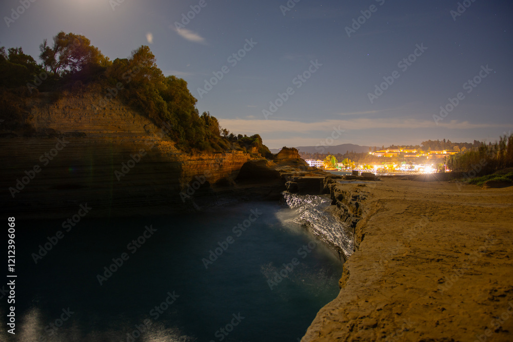 Night scene of ocean waves crashing against rocky cliffs, illuminated by moonlight and distant city lights. Night scene of ocean waves crashing against rocky cliffs, illuminated by moonlight and distant city lights.