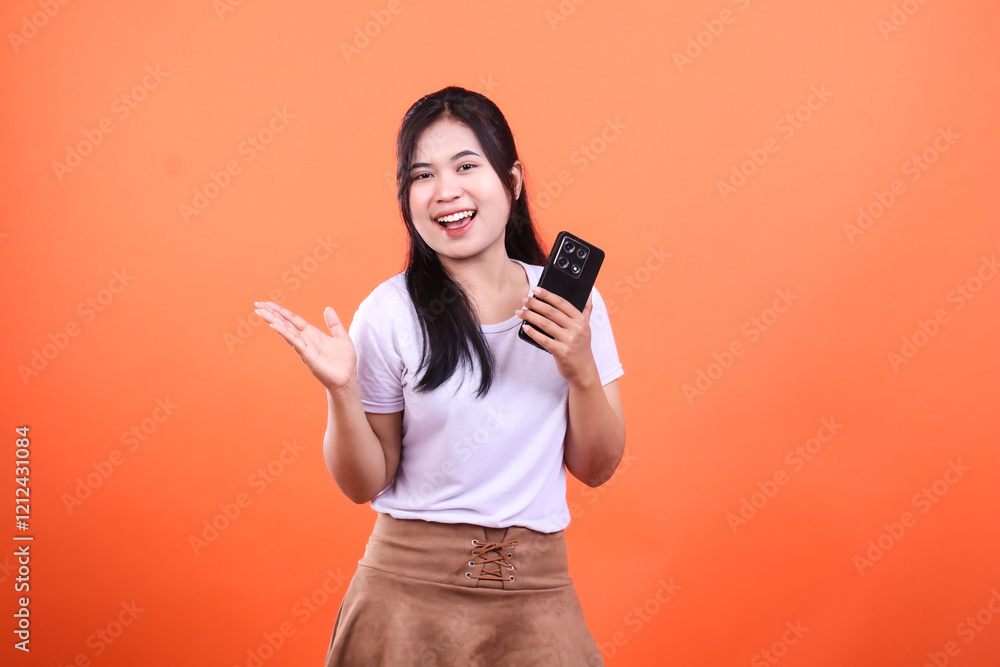 A smiling woman holding a smartphone with her hand open on an orange background A smiling woman holding a smartphone with her hand open on an orange background