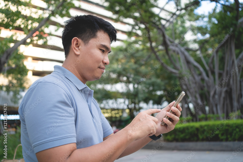 A man is looking at his cell phone in a park. He is wearing a blue shirt and he is focused on his phone A man is looking at his cell phone in a park. He is wearing a blue shirt and he is focused on his phone