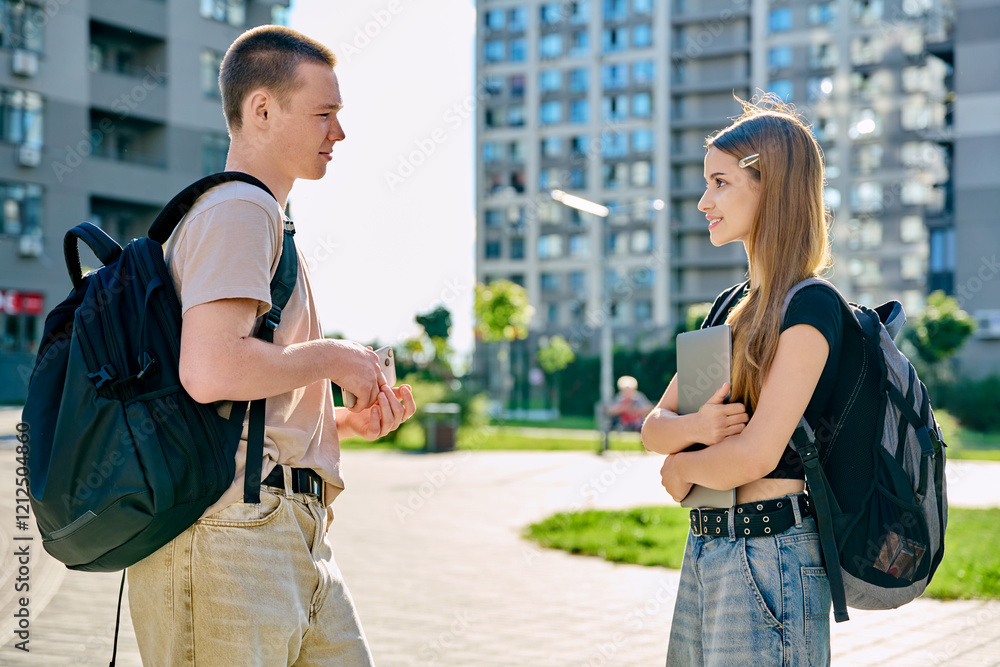 Fototapeta premium College students teenagers guy and girl with backpacks talking together, outdoor