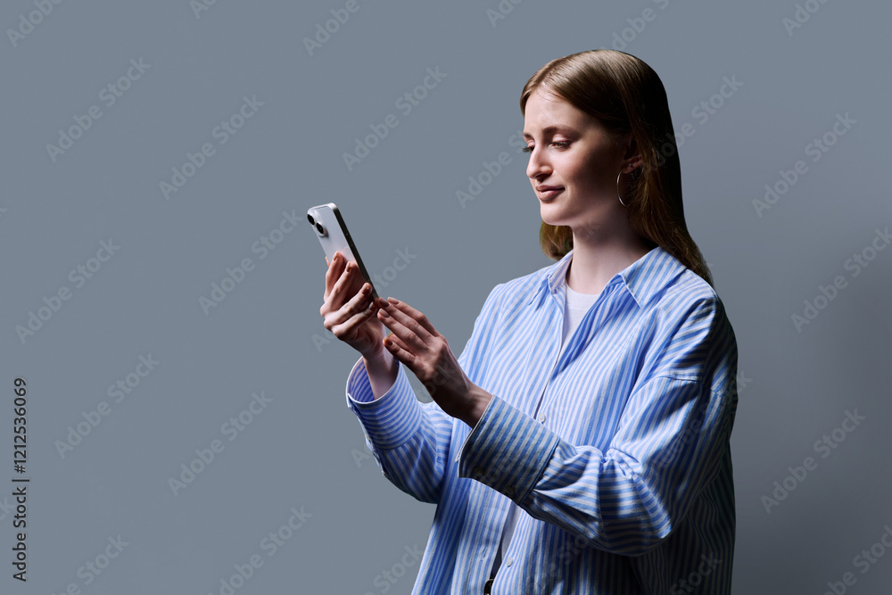 Teenage student girl in blue shirt holding smartphone in hands on grey studio background Teenage student girl in blue shirt holding smartphone in hands on grey studio background