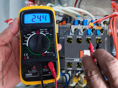 Photography The electrician is measuring the voltage of a magnetic contactor with a digital multimeter to check the device