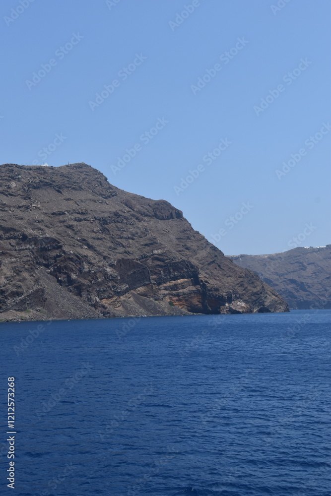 The volcanic crater and rocks of Santorini Island rising from the blue Mediterranean Sea The volcanic crater and rocks of Santorini Island rising from the blue Mediterranean Sea