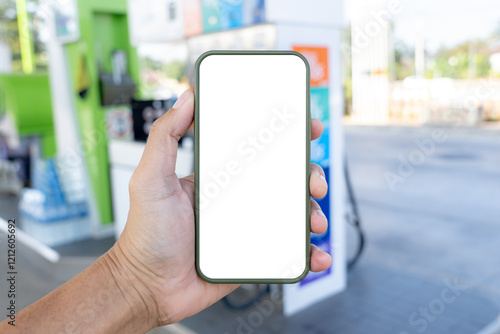 A hand holding a smartphone with a blank screen  with a gas station in the background