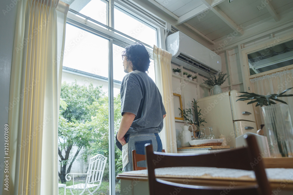 Asian man enjoying a quiet moment by the window in a kitchen, with greenery outside. Asian man enjoying a quiet moment by the window in a kitchen, with greenery outside.