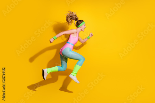 Energetic young woman in retro fitness attire jumping against vibrant yellow background, embodying active lifestyle