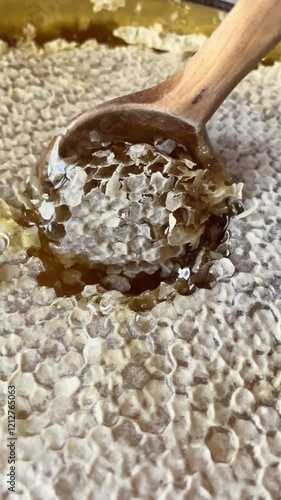 Close-up of a honeycomb with golden honey being scooped with a wooden spoon