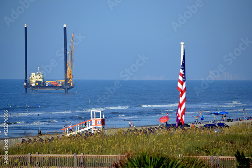 Quadro em tela Near North Myrtle Beach in South Carolina, a dredge is perched on spuds in the water close to the shore, engaged in an erosion restoration effort while beachgoers frolic on the sandy beach and ocean