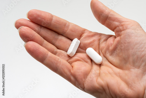 Close-up of female open palm holding two white magnesium tablets or other dietary supplements and medicines. Concept of taking vitamins and minerals supplements to maintain health.