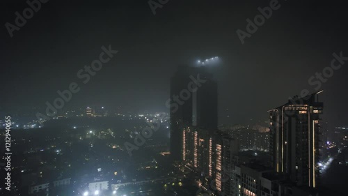 Aerial drone night shot flying towards lit skyscrapers trump towers Spaze Kallista covered in fog haze showing the cityscape and polluted winters of delhi, noida, gurgaon, bangalore