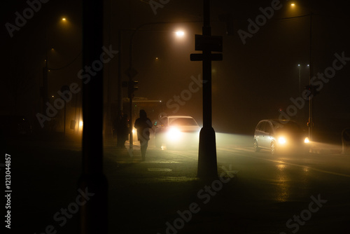 Night intersection with cars, bus and pedestrians illuminated by orange sodium vapour street lamps