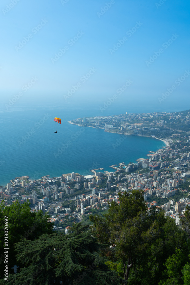 Fototapeta premium A breathtaking aerial view of Jounieh’s seaside with resorts, boats, and paragliders over the blue Mediterranean. Travel blogs, brochures, and adventure magazines.