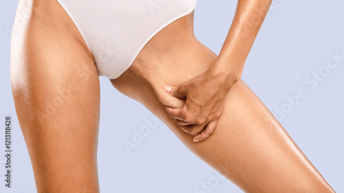 Skin Elasticity Check Concept. Closeup cropped view of unrecognizable young woman pinching her inner thigh, examining cellulite, wearing white panties isolated over blue studio background, banner