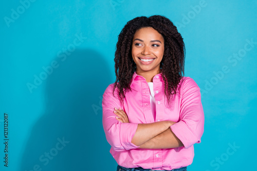 Charming young woman in a pink shirt with curly hair smiling against a vibrant blue background, exuding confidence and style. photo