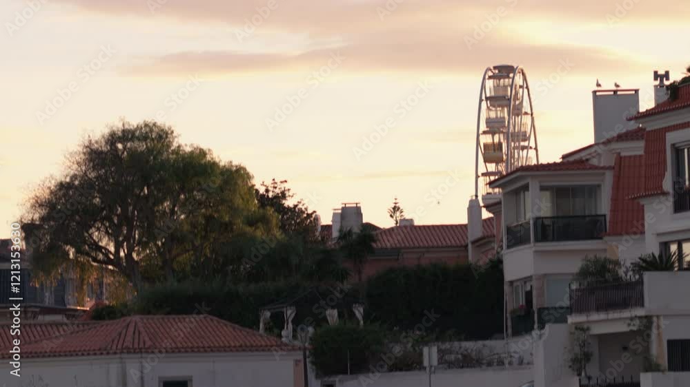 Residential homes against a vibrant sunset in Cascais. Ferris wheel stands prominently, adding charm to the scene, located near the coast Residential homes against a vibrant sunset in Cascais. Ferris wheel stands prominently, adding charm to the scene, located near the coast