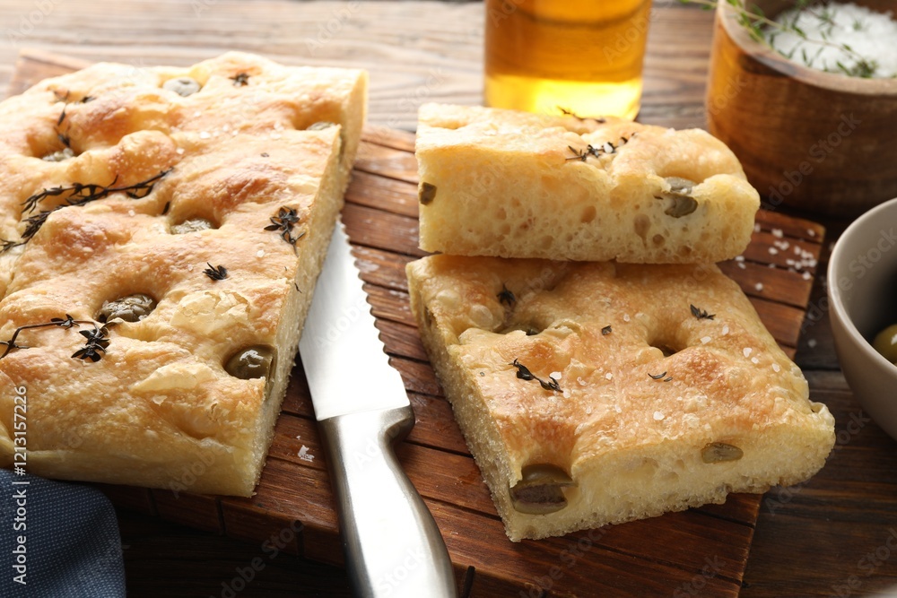 Pieces of delicious focaccia bread with olives, thyme, salt and knife on wooden table, closeup Pieces of delicious focaccia bread with olives, thyme, salt and knife on wooden table, closeup