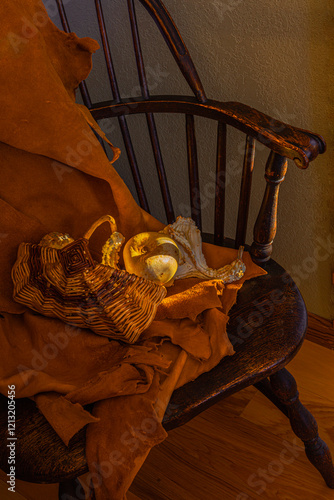 Mottled lighting shines on Native American Indian basket, 1940s, antique Windsor chair, deerskin & gourds. Closeup shows wood rungs & arms of chair in shadow with edge lighting.