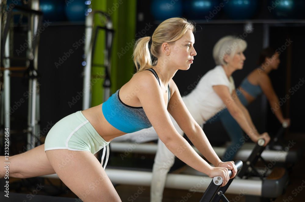 Young woman standing on foldable pilates bed reformer. Athlete participates in pilates training. Strength workout using sports equipment Young woman standing on foldable pilates bed reformer. Athlete participates in pilates training. Strength workout using sports equipment