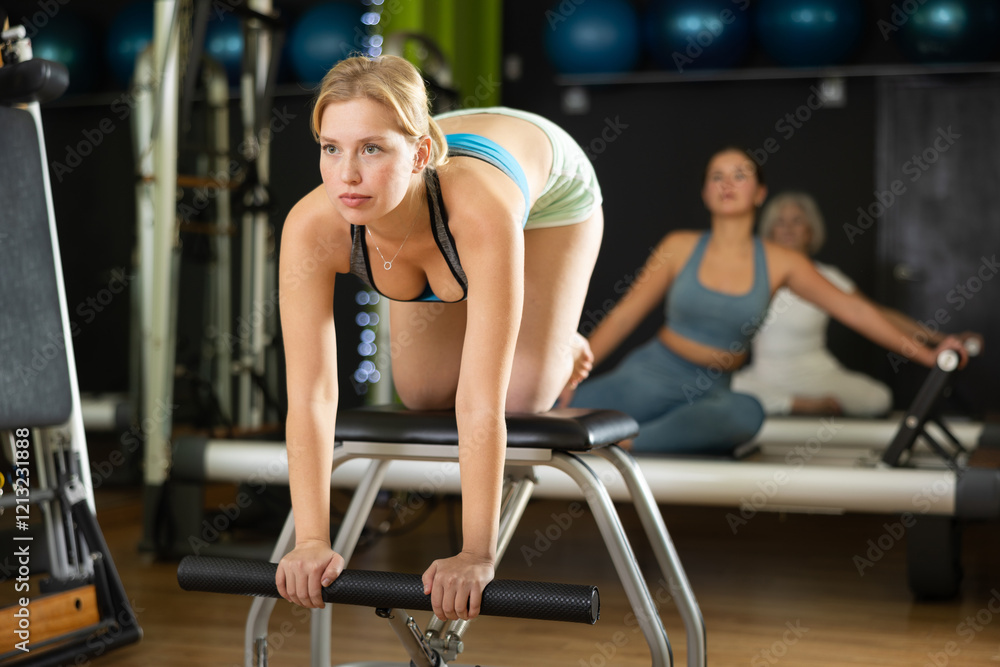 Young woman doing arm exercises on a Pilates chair. Visitor uses special equipment in the Pilates studio Young woman doing arm exercises on a Pilates chair. Visitor uses special equipment in the Pilates studio