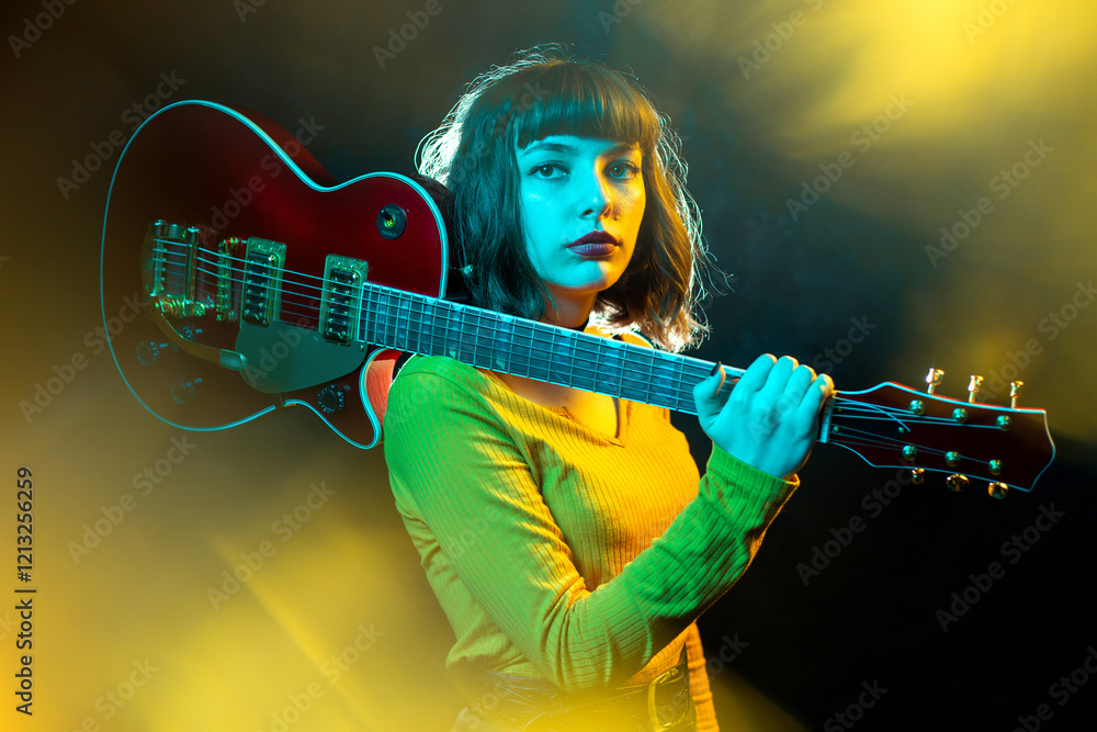 Obraz premium Hipster woman with curly hair play red guitar in neon lights. Rock musician is playing electrical guitar.