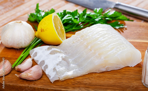 Raw pink cusk-eel fillet, garlic, parsley and lemon on wooden table. Ingredients for cooking photo