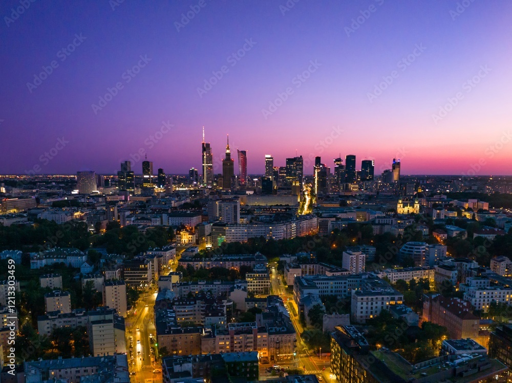 Obraz premium City skyline of Warsaw illuminated at dusk with a vibrant sky and busy streets below showcasing urban life