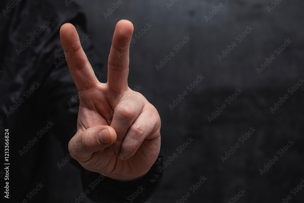 Man in a shirt showing gesture V means victory, peace sign or protest sign, close-up against on dark background.