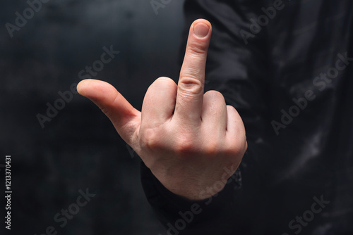 Obraz na płótnie Man in a shirt showing a crude fuck gesture, middle finger sign, close-up against a concrete wall