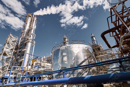 The distillation column at a modern chemical plant under a clear blue sky with steam rising, reflecting industrial activity and innovation