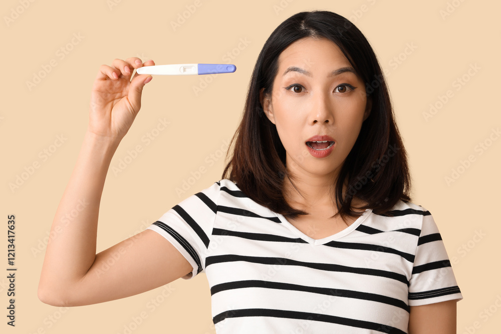 Shocked beautiful young Asian woman with pregnancy test on beige background Shocked beautiful young Asian woman with pregnancy test on beige background