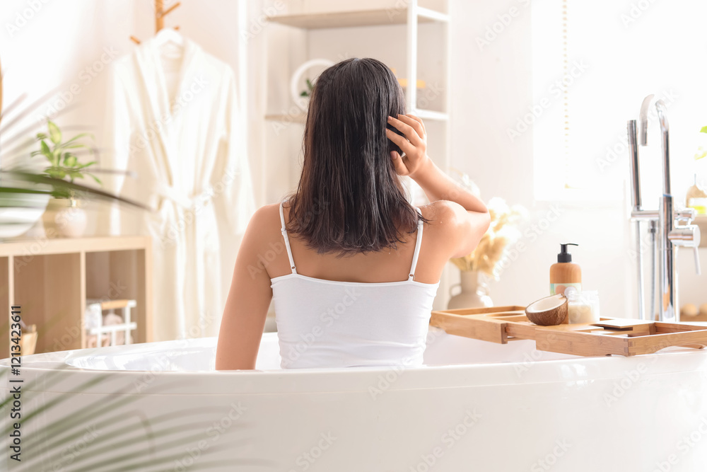 Pretty young woman applying coconut oil on her hair in bathroom, back view Pretty young woman applying coconut oil on her hair in bathroom, back view
