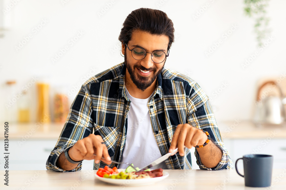 Positive arab guy hipster having healthy breakfast at home, eating fresh vegetables, sausages, drinking coffee, sitting at kitchen table, copy space. Handsome indian man starting day with nice meal Positive arab guy hipster having healthy breakfast at home, eating fresh vegetables, sausages, drinking coffee, sitting at kitchen table, copy space. Handsome indian man starting day with nice meal