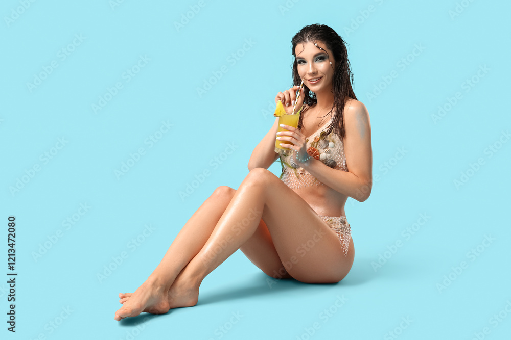 Naklejka premium Beautiful young woman dressed as mythical mermaid with glass of pineapple juice on blue background